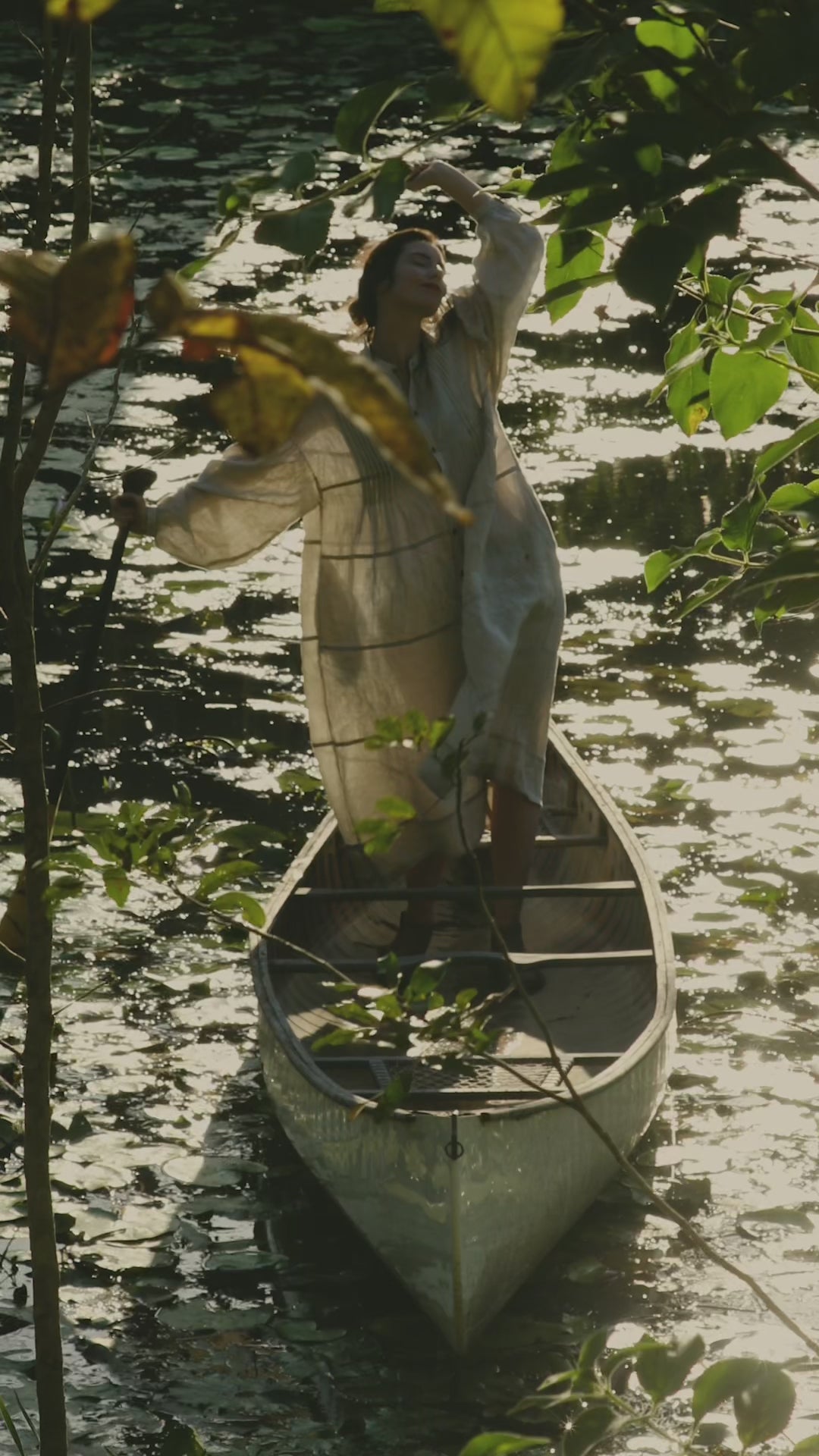 Woman in The Boro Dress Standing in a canoe, out on a pond covered in lilypads.